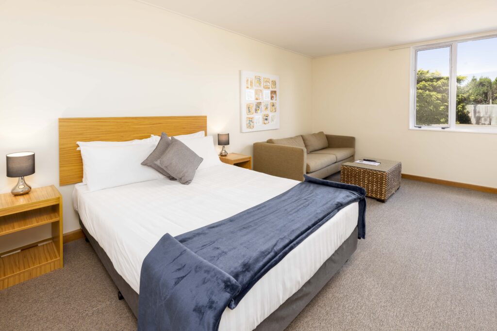 Queen guest room at Methven Resort with modern bed, sofa seating area, and natural light.