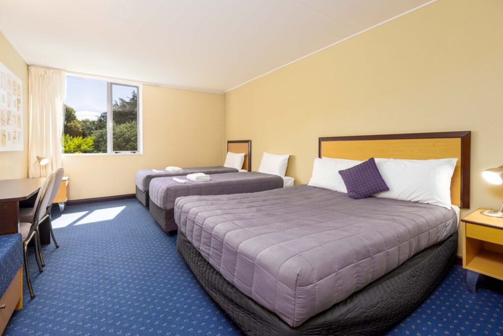 Triple guest room at Methven Resort with one queen bed, two single beds, desk, and window view.