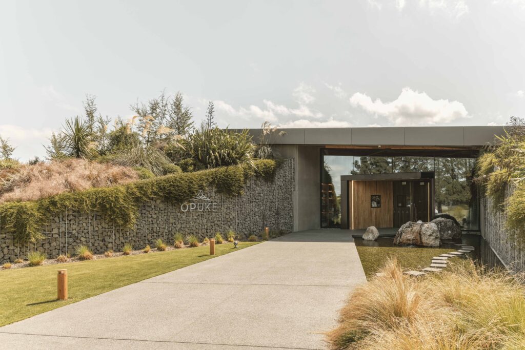 Entrance of Opuke Thermal Pools and Spa in Methven, New Zealand with stone walls, landscaped greenery and modern architecture.