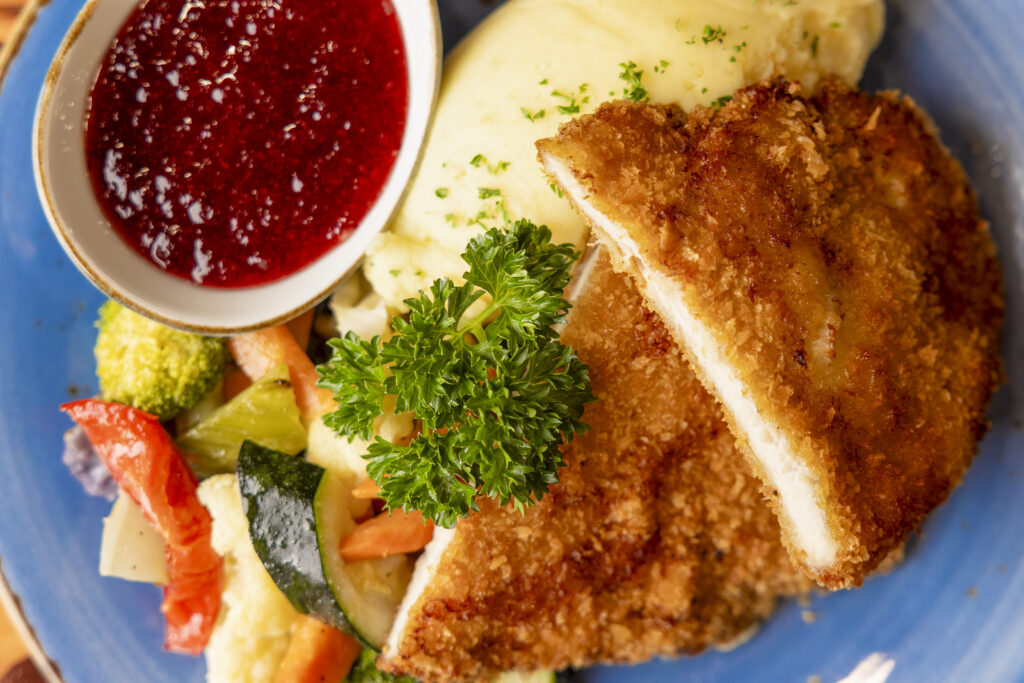Crispy schnitzel served with mashed potato, roasted vegetables, parsley garnish, and cranberry sauce at Methven Resort restaurant.
