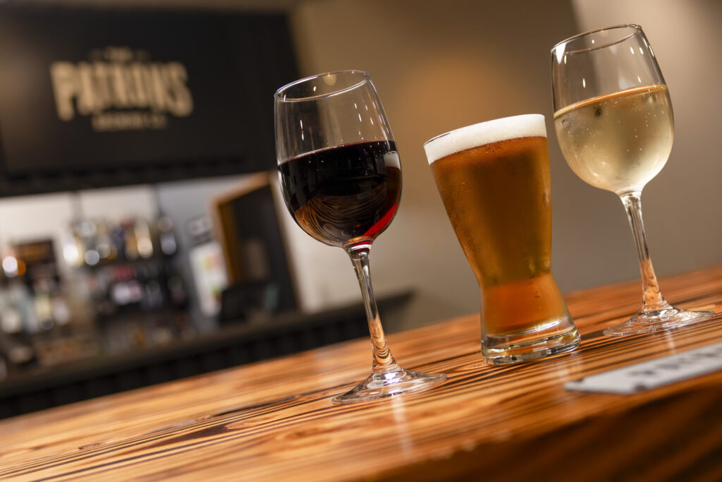 Glasses of red wine, white wine, and beer served on wooden bar counter at hotel lounge.