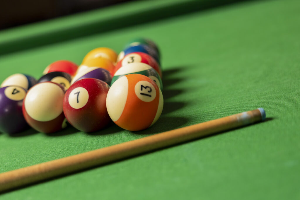 Close-up of billiard balls arranged in a triangle with a pool cue on green table.