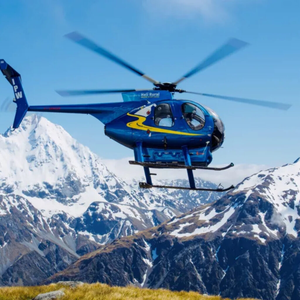 Blue helicopter flying over snow-capped Southern Alps in Canterbury, New Zealand.