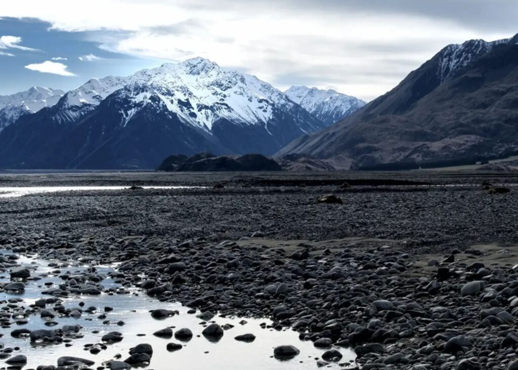 Snow-covered Southern Alps mountains with rocky riverbed foreground in Canterbury, New Zealand.